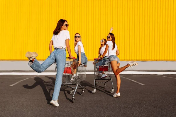 快乐的年轻女人穿着休闲装 朋友们玩得开心 坐着购物车 在购物中心的背景下 — 图库照片