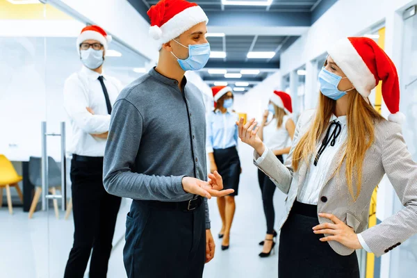 team of business people in medical protective masks on faces and red caps of Santa Claus communicating in the office, Christmas, coronavirus, quarantine