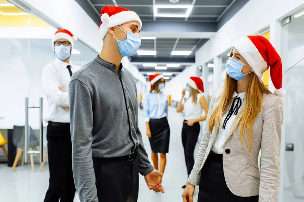 team of business people in medical protective masks on faces and red caps of Santa Claus communicating in the office, Christmas, coronavirus, quarantine