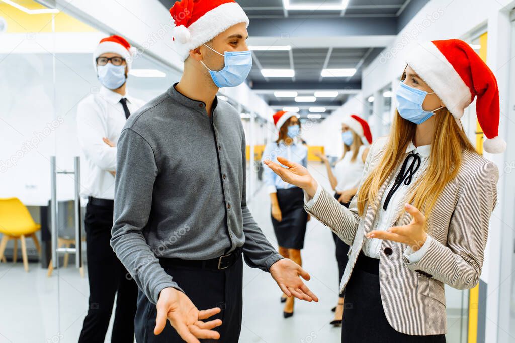 team of business people in medical protective masks on faces and red caps of Santa Claus communicating in the office, Christmas, coronavirus, quarantine
