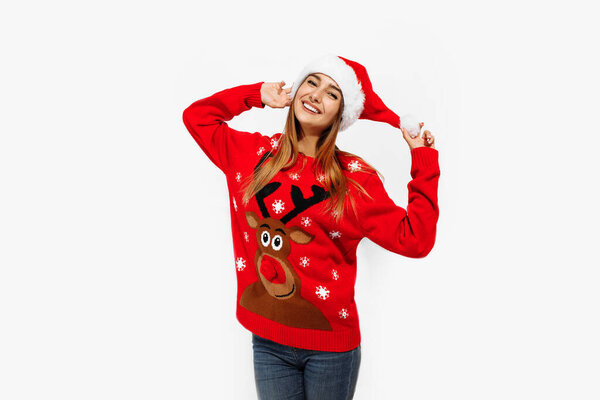 Happy cute young woman in christmas sweater and santa claus hat, on white background