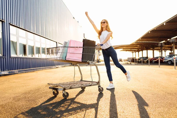 快乐快乐的年轻女性喜欢购物 她背着购物袋 开着购物车在商场附近的城市里跑来跑去 — 图库照片