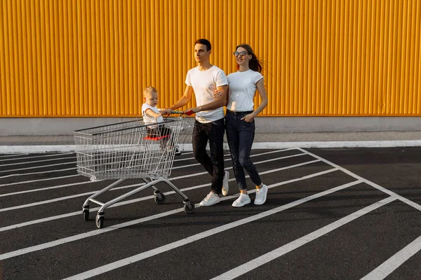幸福的家庭 丈夫和妻子 孩子们坐在购物车里 靠着购物中心的黄墙购物 — 图库照片