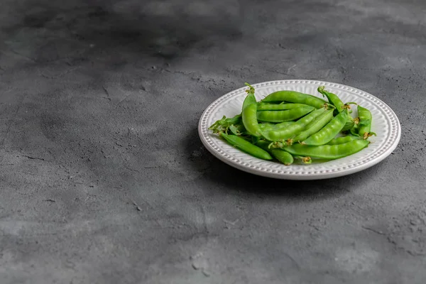taze yeşil bezelye, koyu arka planda seramik beyaz plaka