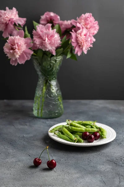 koyu arka planda pembe şakayık çiçeği buket, kiraz ve yeşil bezelye