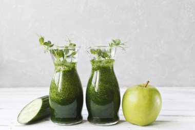 İki bardak Close-Up taze ev yapımı meyve suyu salatalık, elma ve bezelye ile beyaz ahşap zemin üzerine bırakır. Alan, seçici odak sığ derinliği