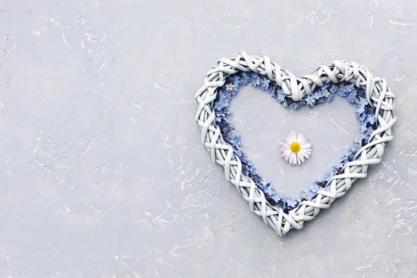 Close-up photo of cute heart shape with blue little flowers on gray table background. Top view