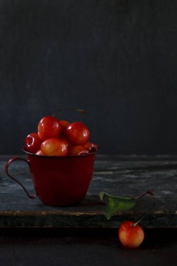 Fotoğraf kırmızı taze kiraz çilek kırmızı kupa tablosunda yakın. Ülke vintage tarzı, arka plan, makro.