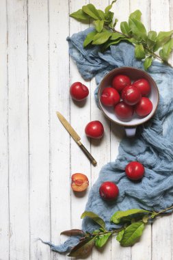 Bir kase taze kırmızı erik yakın çekim fotoğraf. Beyaz vintage ahşap zemin üzerinde üstten görünüm.