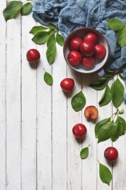 Bir kase taze kırmızı erik yakın çekim fotoğraf. Beyaz vintage ahşap zemin üzerinde üstten görünüm.