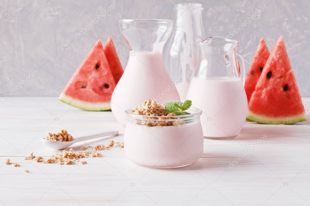 Fruit yogurt, smoothies in jug, granola and sliced watermelon on white wooden background. 