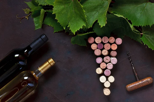 Red and white wine in bottles, corks, corkscrew and grape leaves. Top view, close up on dark vintage background