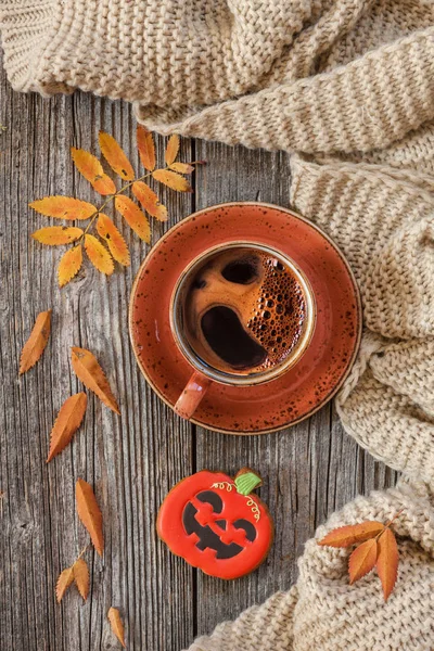 Cup of hot black coffee and pumpkin gingerbread with leaves and warm scarf on wooden table, top view