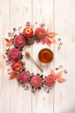 Apples, pink flowers and  honey with copy space form a floral decoration. Concept for Rosh Hashanah the Jewish New Year, harvest festival, Lammas. Top view, close up on white wooden background