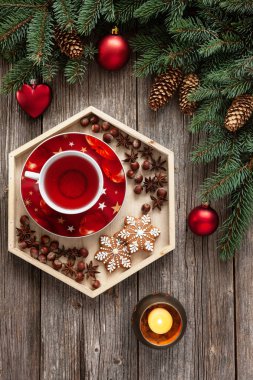 köknar ağacı dalları, koniler, mum, Noel süsleri ve kırmızı çay ile gingerbread kar taneleri üzerinde ahşap masa, üstten görünüm