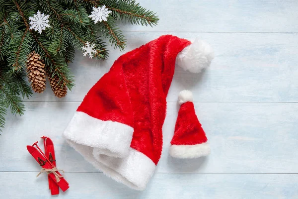 モミの木の枝 コーン 装飾的なスキーと つのサンタ クロースの帽子とクリスマスの背景 クリスマスと新年のコンセプトです ライト ブルー木製テーブル あなたのテキストのための場所のクローズ アップ — ストック写真