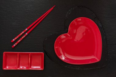 Kırmızı kalp şekli plaka üstten görünüm ile chopsticks ve fincan tabağı siyah taş zemin üzerine siyah taş gemide
