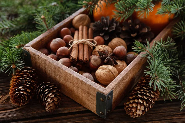 Walnuts, hazelnuts, cones, oranges  in the wooden box on rustic wooden background with fir tree branches and Christmas lights. Close up, selective focus