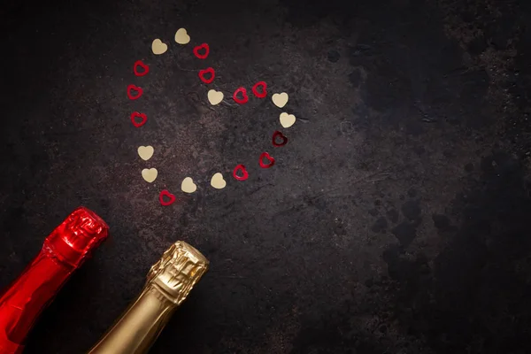 Two bottles of champagne and pattern of red and gold hearts. Top view, close-up, flat lay on dark brown background
