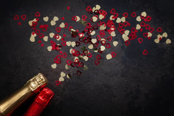 Two bottles of champagne and pattern of red and gold hearts. Top view, close-up, flat lay on dark brown background