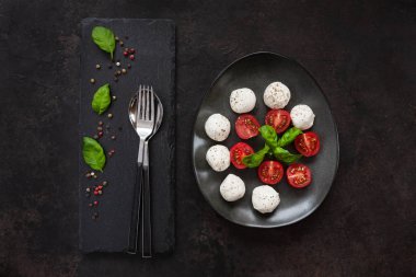 Beyaz mozzarella topu peyniri, kırmızı kiraz domates, zeytin yağı ve fesleğen karanlık beton zemin üzerine yakın çekim. Üstten görünüm, düz yatıyordu