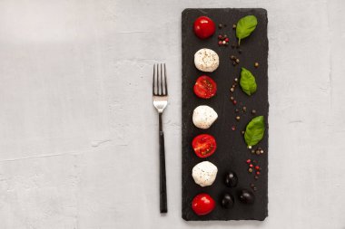 Beyaz mozzarella topu peyniri, kırmızı kiraz domates, zeytin yağı ve fesleğen hafif beton zemin üzerine yakın çekim. Üstten görünüm, düz yatıyordu