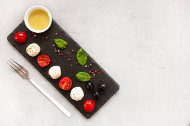 Beyaz mozzarella topu peyniri, kırmızı kiraz domates, zeytin yağı ve fesleğen hafif beton zemin üzerine yakın çekim. Üstten görünüm, düz yatıyordu