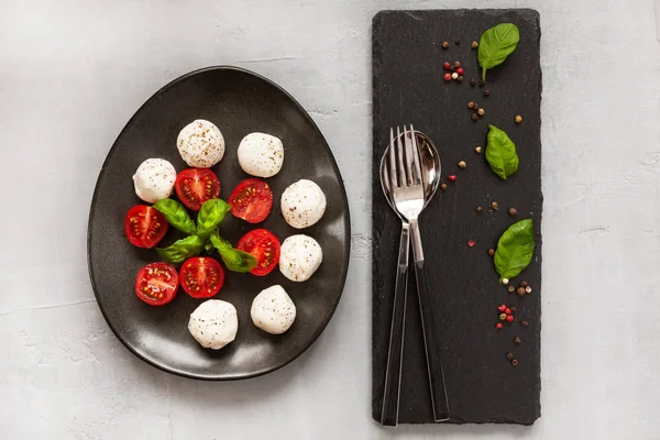 Beyaz mozzarella topu peyniri, kırmızı kiraz domates, zeytin yağı ve fesleğen hafif beton zemin üzerine yakın çekim. Üstten görünüm, düz yatıyordu