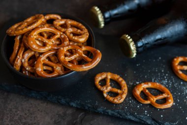 İki şişe bira ve koyu taştan arka planda tuzlu bretzel.