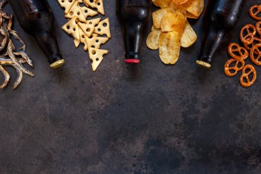 Üç şişe bira, cips, tuzlanmış kraker, bretzel ve kurutulmuş eritilmiş balık.