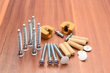 Euro screws, dowels, ties, chrome-plated pipe and console are laid out on a wooden panel clipart