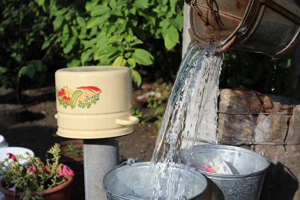 photo water from a bucket / water poured from a bucket.the well in the village.the liquid is clean and transparent.in the yard.five-liter pan yellow.the yard is private property.time year summer,day.sunny weather.