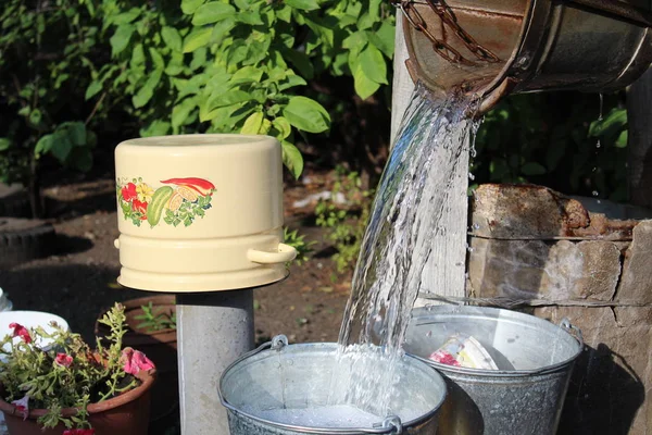 photo water from a bucket / water poured from a bucket.the well in the village.the liquid is clean and transparent.in the yard.five-liter pan yellow.the yard is private property.time year summer,day.sunny weather.