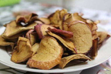 Elma meyveleri yaz mevsiminde evde kurutuldu / kurutulmuş meyvelerin yakın plan fotoğrafı. Ev mutfağında kurutulmuş elmalar. Masanın üzerinde bir tabağın üzerindeler..