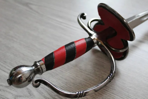 El yapımı kılıç kabzası. Sanatsal eskrim için yakın plan. Kılıç kabzasının yakın plan fotoğrafı. Paslanmaz çelikten yapılmış soğuk silahlar. Kapı kolu kırmızı ve siyah deriyle süslenmiş..
