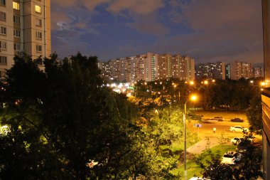 Moskova şehrinin güzel gece manzarası ve şehir manzarası. Moskova şehri, akşam caddeleri. Yolda arabalar var. Yazın yeşil yapraklı ağaçlar. Yüksek binaların pencerelerinde ışıklar vardır..