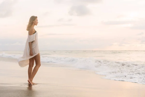 カジュアルな夏の流行に敏感なおしゃれな女性は喫水線で裸足で歩くドレス 波に見えます 海砂のビーチの夕日や海の日の出にスポーティな女性 アクティブなヨガのライフ スタイル コンセプト — ストック写真