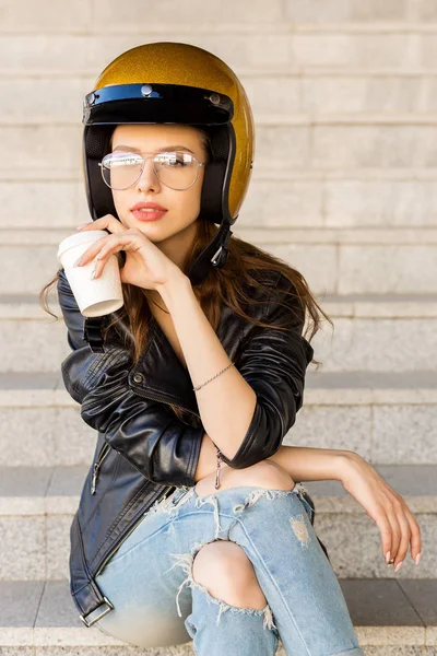 美しい若い女性ファッションのメガネ 岩黒革ジャケットとキラキラ金バイク ヘルメットお茶を飲む空白のホワイト ペーパー カップから 流行に敏感な都会的なスタイルの女の子 ライフ スタイル屋外都市の肖像画 — ストック写真