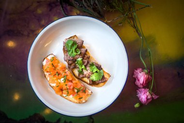 Bir restoranda beyaz tabakta iki bruschetta. Balık ve et