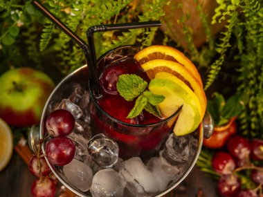 Buzlu bir kovada kırmızı alkollü kokteyl. Ahşap bir masada meyve ve çilek ile süslenmiş.