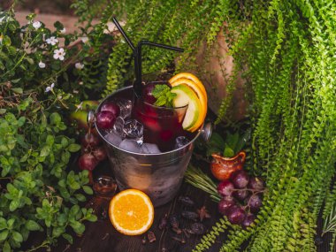 Buzlu bir kovada kırmızı alkollü kokteyl. Ahşap bir masada meyve ve çilek ile süslenmiş.