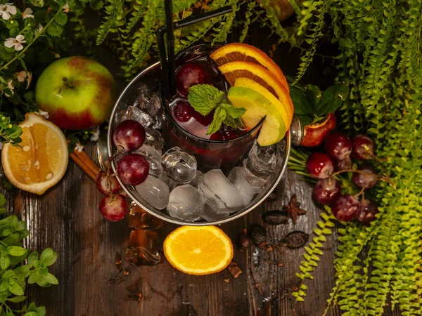 Red alcoholic cocktail in a bucket with ice. Garnished with fruits and berries on a wooden table. — Stock Photo, Image