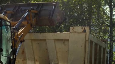 Bir traktör yeni asfalt döşemeden önce, bir konut binanın avlusında inşaat enkaz kaldırır. Güneşli yaz günü.