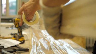 Marangozluk atölyesinde bir zanaatkar, kelepçelerle tutturan tahtalara lastik çekiçle vuruyor.