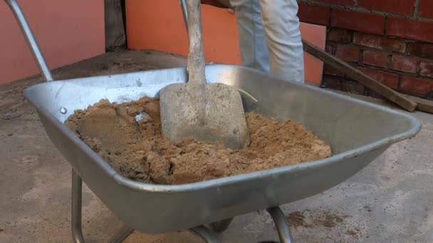 Ein Mann Schaufelt Sand Von Einem Wagen Für Einen Betonmischer — Stockvideo