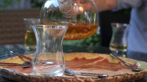 Un homme verse du thé chaud d'une théière en verre dans une tasse transparente. Thé sain à base de plantes 