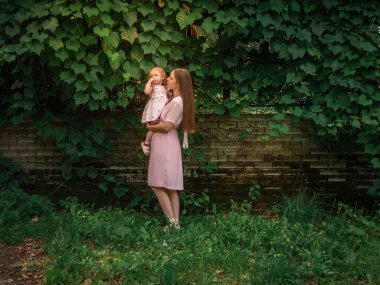 Anne ve kızı parkta yürüyüp oynuyorlar. Elbise giymişti. Güneşli bir gün, hafta sonu şehir parkında.