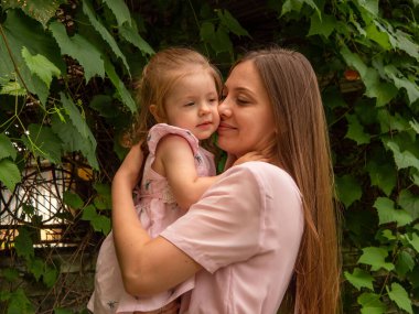 Anne ve kızı parkta yürüyüp oynuyorlar. Elbise giymişti. Güneşli bir gün, hafta sonu şehir parkında.