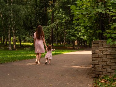 Anne ve kızı parkta yürüyüp oynuyorlar. Elbise giymişti. Güneşli bir gün, hafta sonu şehir parkında.