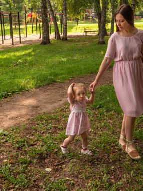 Anne ve kızı parkta yürüyüp oynuyorlar. Elbise giymişti. Güneşli bir gün, hafta sonu şehir parkında.